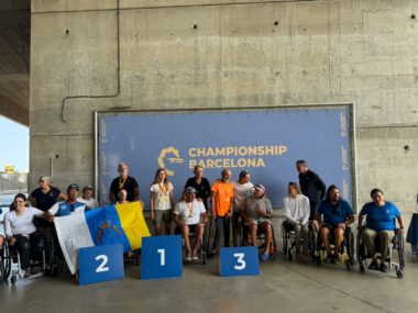 Pòdium del Campionat de Catalunya de Hansa 303 amb els guanyadors, regatistes en cadires de rodes i adaptats, en una cerimònia de lliurament de premis amb fons blau i logotip del campionat.