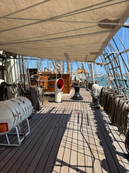 Vista de la coberta principal del Clipper Stad Amsterdam amb el timó, l’aparell de navegació tradicional i les maniobres del vaixell atracat al port.
