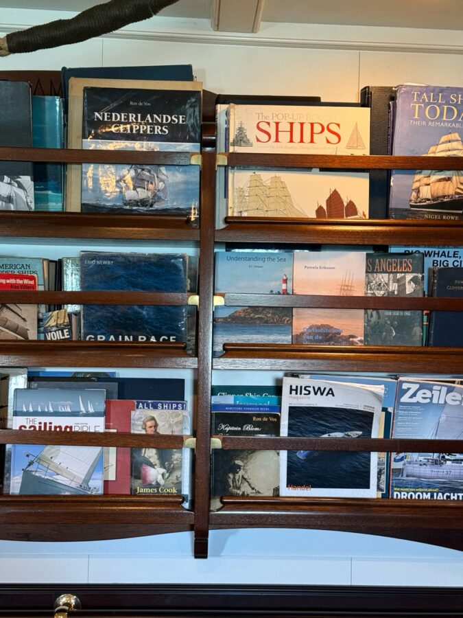 Prestatgeria de fusta a l’interior del Clipper Stad Amsterdam amb llibres i revistes especialitzades en navegació, història marítima i grans velers.