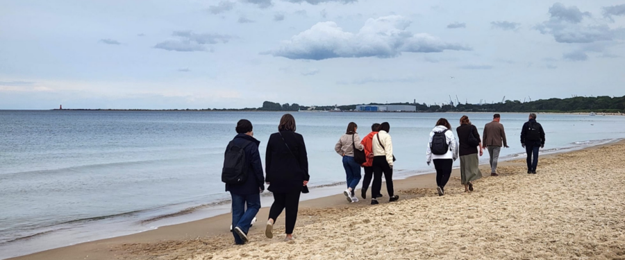 Un grup de persones camina per la platja de Gdańsk durant una visita de treball sobre educació marítima i resiliència juvenil.