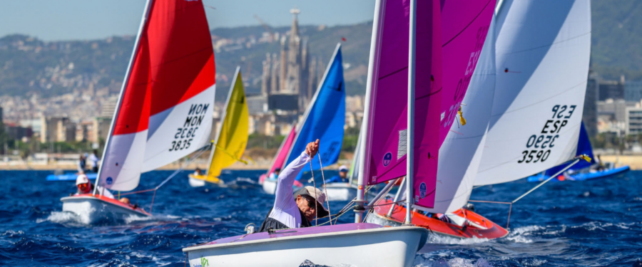 Un regatista en una embarcació Hansa durant el Campionat d’Europa Hansa 2026 a Barcelona, amb altres velers al fons i la ciutat de Barcelona de fons.